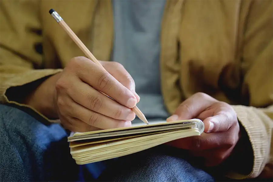 A man's hand with pencil writing in a notebook, brainstorming ideas.